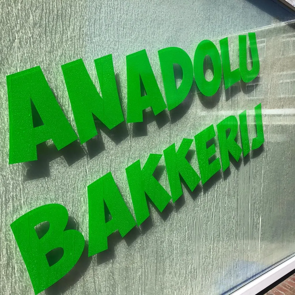 Groene reliëf-raambelettering met de naam Anadolu Bakkerij op de etalageruit van de bakkerij.